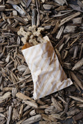 Banana, apple and blueberry bone-shaped dog treats in a striped paper bag on wood chips.