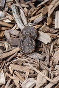 Two dark brown, textured beef burger dog treats stacked on top of natural wood chips.
