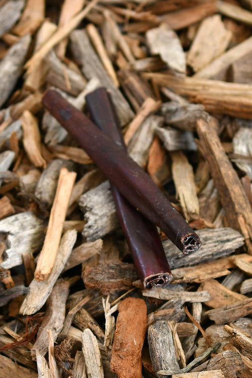 Two beef collagen sticks resting on wood chips and bark pieces.