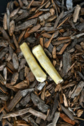 Two pale yellow beef tail chews lying on a bed of wood chips.
