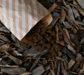 Bone-shaped rabbit and ostrich training treats spilling from a striped paper bag onto wood chips.