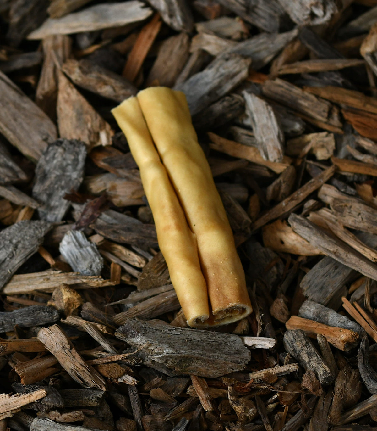 Deer hide roll dog chew treat placed on a bed of wood chips and bark.