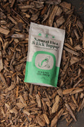 Natural flea and tick topper for dogs in a green and white pouch, placed on a bed of rustic wood chips.