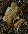 Natural hairy beef skin dog chew displayed on a bed of dark wood chips.