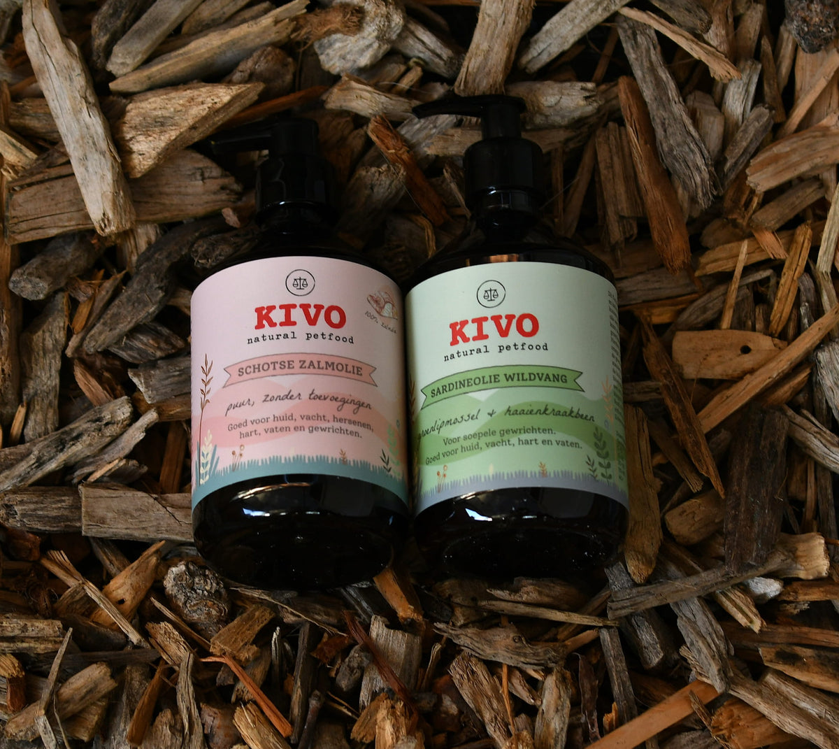 Two KIVO natural pet food oil bottles, one containing salmon oil and one containing sardine oil, placed side by side on wood chips.