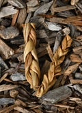 Two braided lamb skin chews lying on a bed of wood chips.