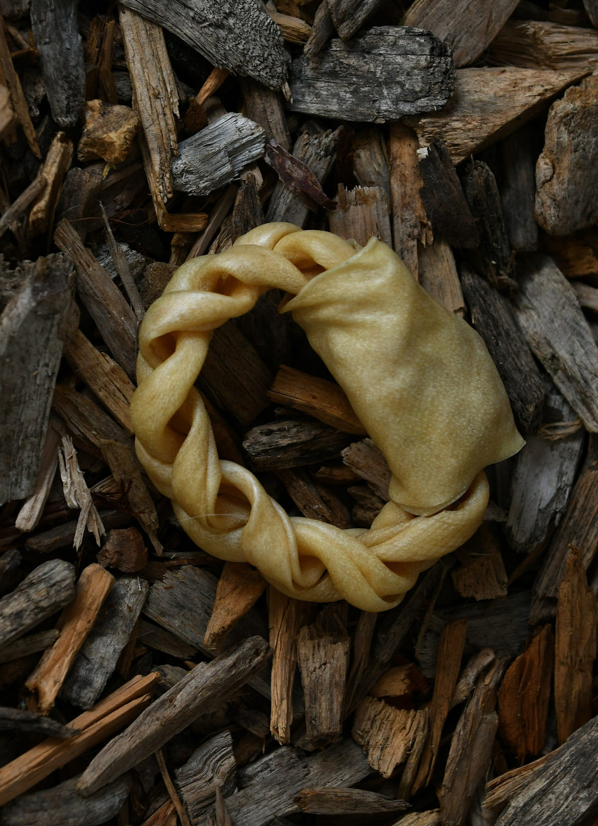 Lamb collagen ring chew displayed on a bed of natural wood chips.