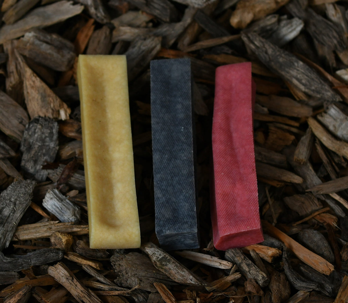 Three yak chews in different flavours and colours, arranged on a bed of rustic wood chips.