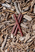 Three red-brown meat sticks crossed in an X shape, with beef, horse and venison varieties, lying on a bed of wood chips.