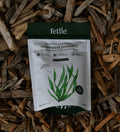 A stand-up pouch of Fettle All-Natural Scottish Kelp Seaweed Powder, featuring a white and dark green design with a green kelp illustration, set against a background of wood chips.