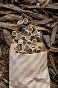 Peanut butter reward coins dog treats in a striped paper bag, displayed on a bed of natural wood chips and bark