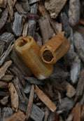 Two rolled pig skin chews with a darker filling visible inside, shown on a natural wood-chip background.