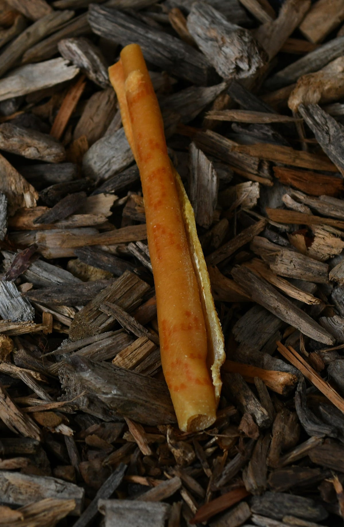 Pork skin roll dog chew on a natural wood-chip background.