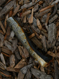 A single salmon skin roll with textured silver-grey skin and a dark underside, shown on a natural wood-chip background.