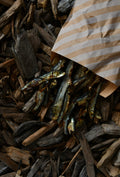 Small dried fish spilling from a brown-and-cream striped paper bag onto dark wood chips.