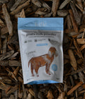 A stand-up pouch of Fettle Natural & Sourced Goats Milk Powder placed on a bed of wood chips. The pouch is white with a light blue top and bottom border, featuring a brown goat illustration and product text.