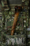 XL ostrich metatarsus bone chew displayed vertically against a camouflage tactical vest.