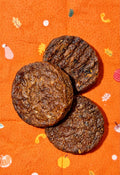 Three round burger treats arranged on an orange fabric background with a small autumn-themed print.