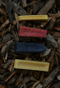 Four yak chews in different flavours and colours, arranged on a bed of rustic wood chips.