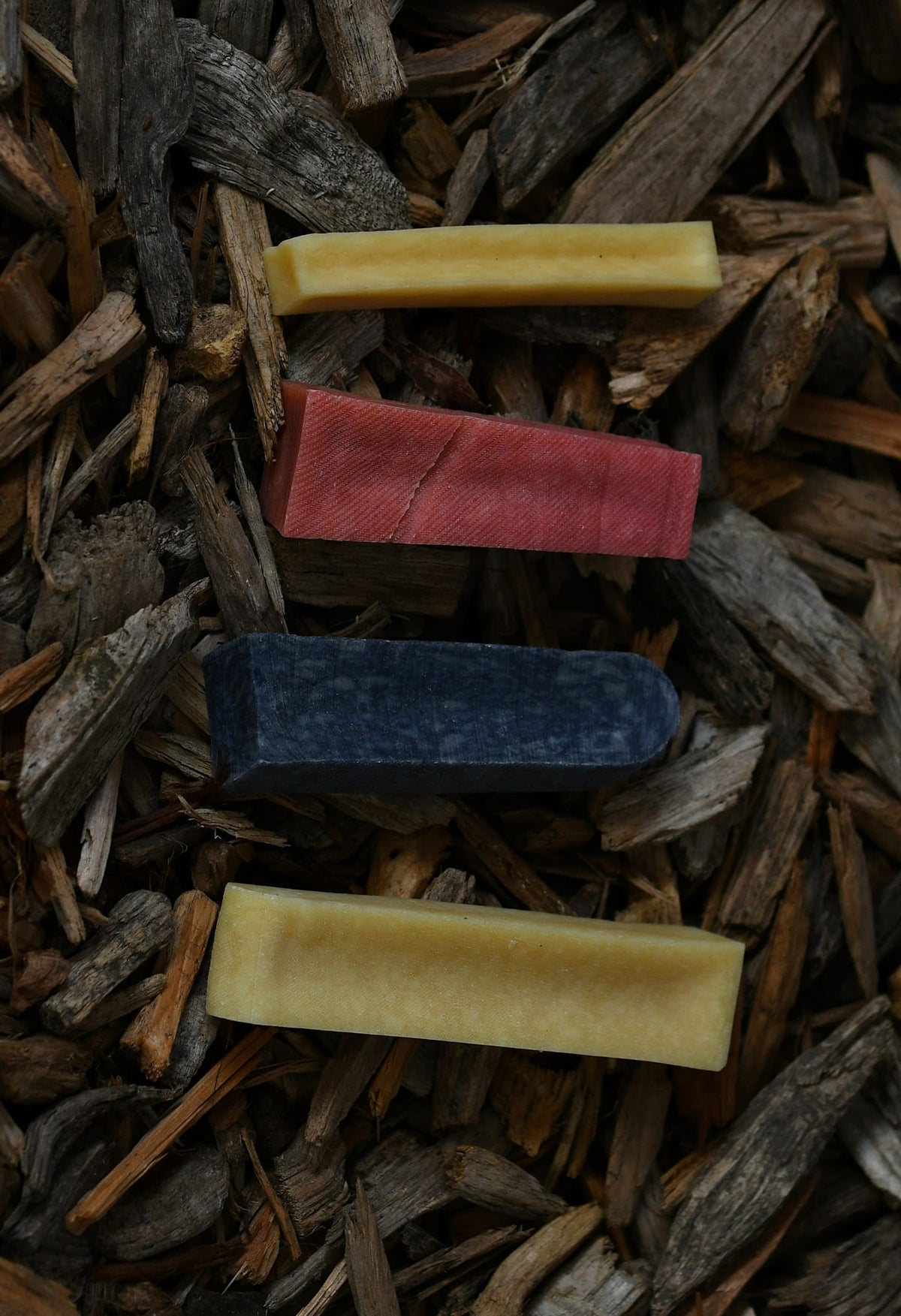 Four yak chews in different flavours and colours, arranged on a bed of rustic wood chips.