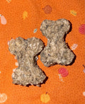 Two bone-shaped dog treats made of textured dried ingredients, placed on an orange patterned fabric background.
